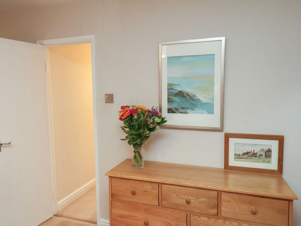 A hallway with flowers on a chest of drawers and paintings on the wall at Farriers Yard, Whitby