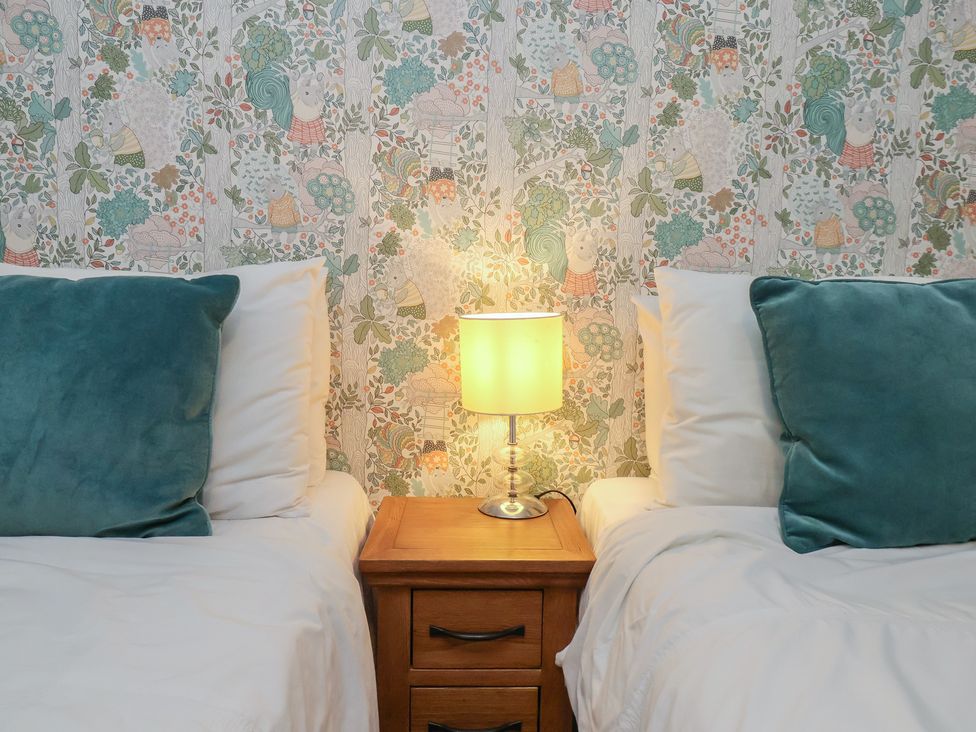 A bedroom with two beds, a lamp on a nightstand and patterned wallpaper at Farriers Yard in Whitby