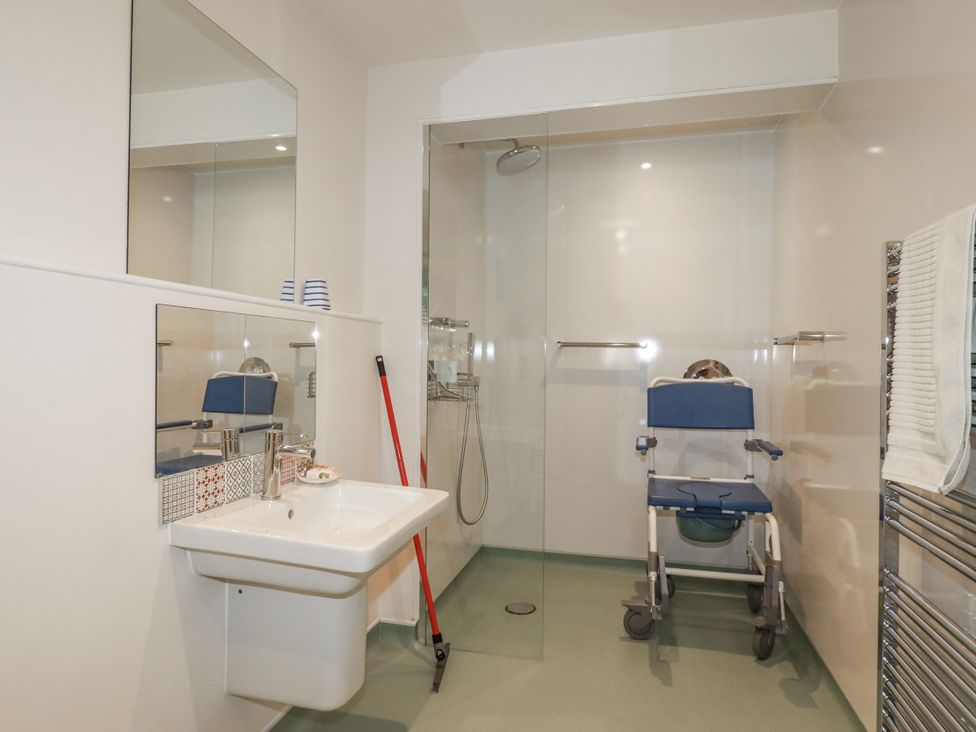 A bathroom with a sink, mirror, shower, and shower chair at Hillbre, Trevone