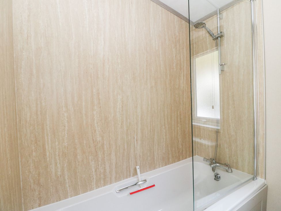 A bathtub with a showerhead and glass screen at Altair Lodge
