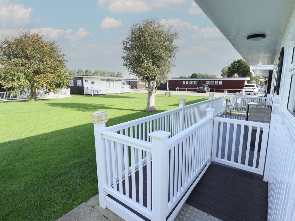 A deck area overlooking grass and mobile homes at No.49 Cherry Park in Chapel St Leonards