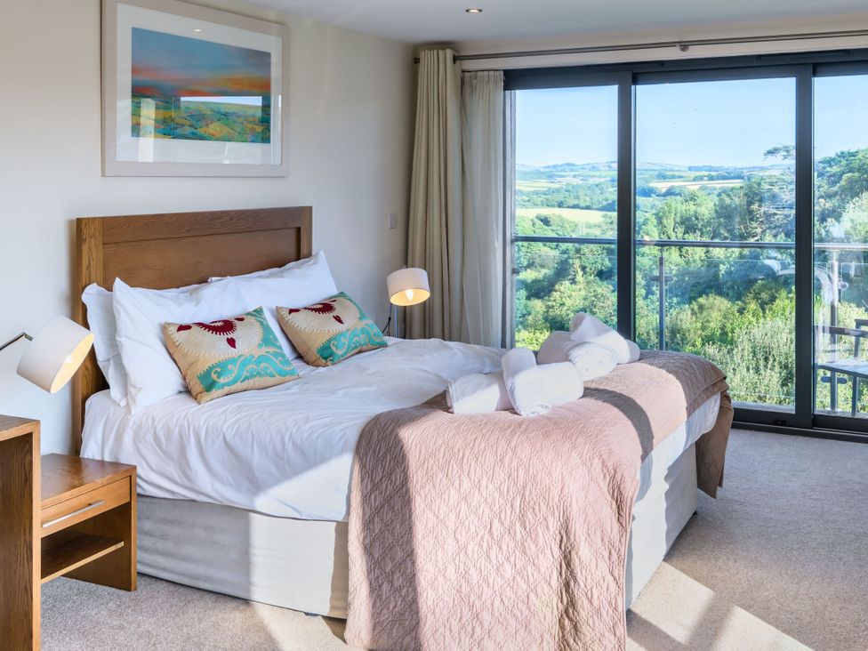 A bedroom with a bed and large windows at Nan's House Spa Marhamchurch