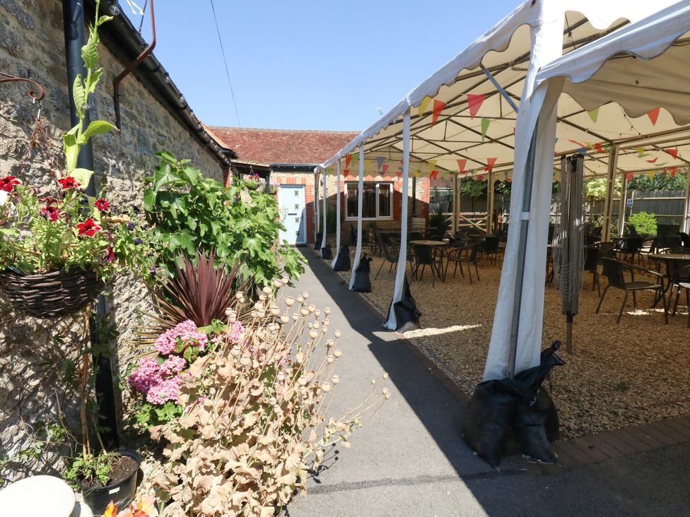 An outdoor area with a pathway, canopy, tables, and flowers at The Old Barn in Stourton Caundle near Stalbridge