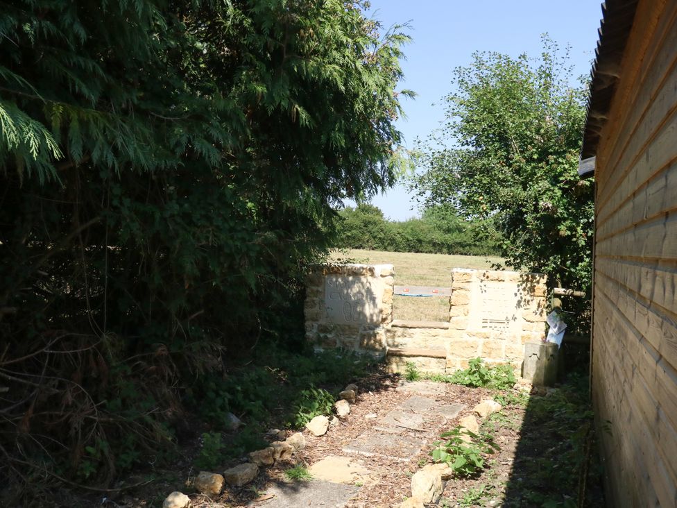 A pathway leading to a stone wall with trees at The Old Barn in Stourton Caundle near Stalbridge