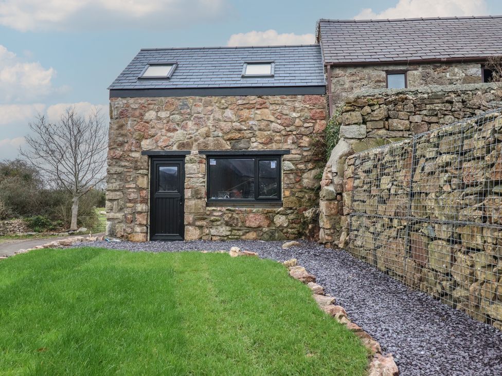 A stone exterior of a house with a lawn and gravel path at Trigfa Brynsiencyn near Llanfairpwllgwyngyll