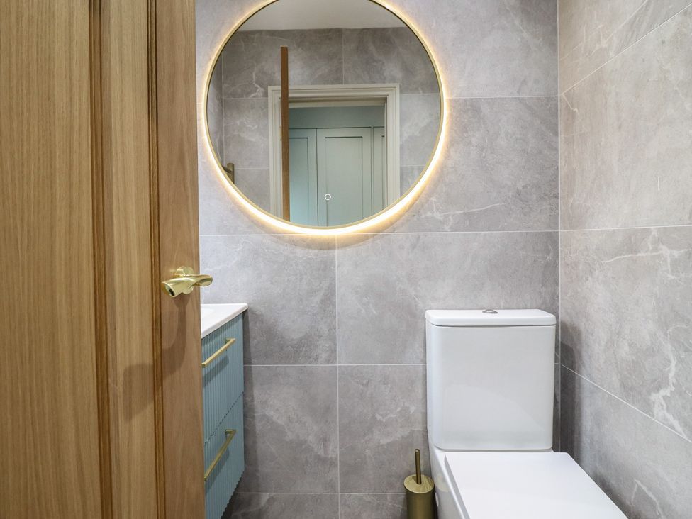 A bathroom featuring a toilet, sink, mirror, and wooden door at Pistyll Ddu in Brynsiencyn near Llanfairpwllgwyngyll