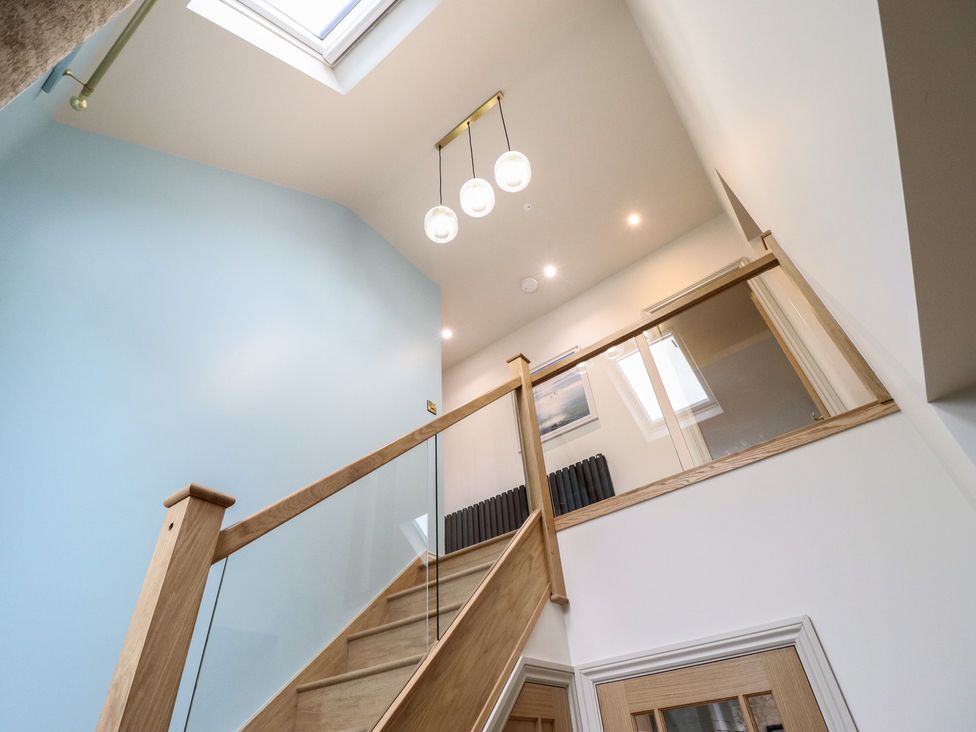 A staircase with a glass railing and light fixtures in a hallway at Pistyll Ddu near Brynsiencyn