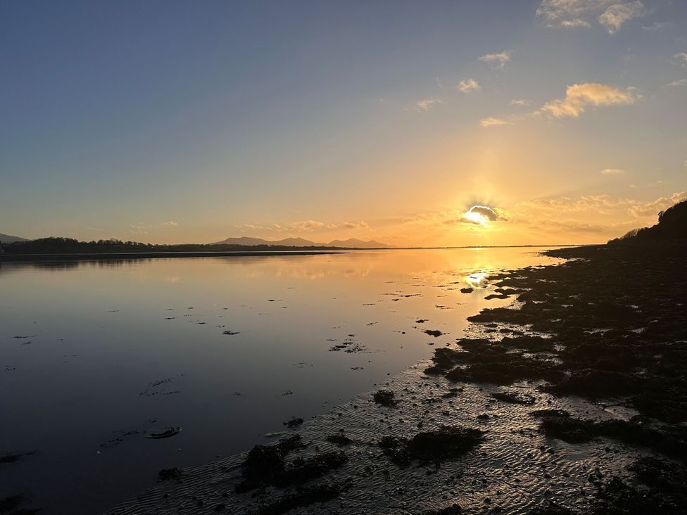 A view of a sunset over water with mountains in the distance at Pistyll Ddu Llanfairpwllgwyngyll