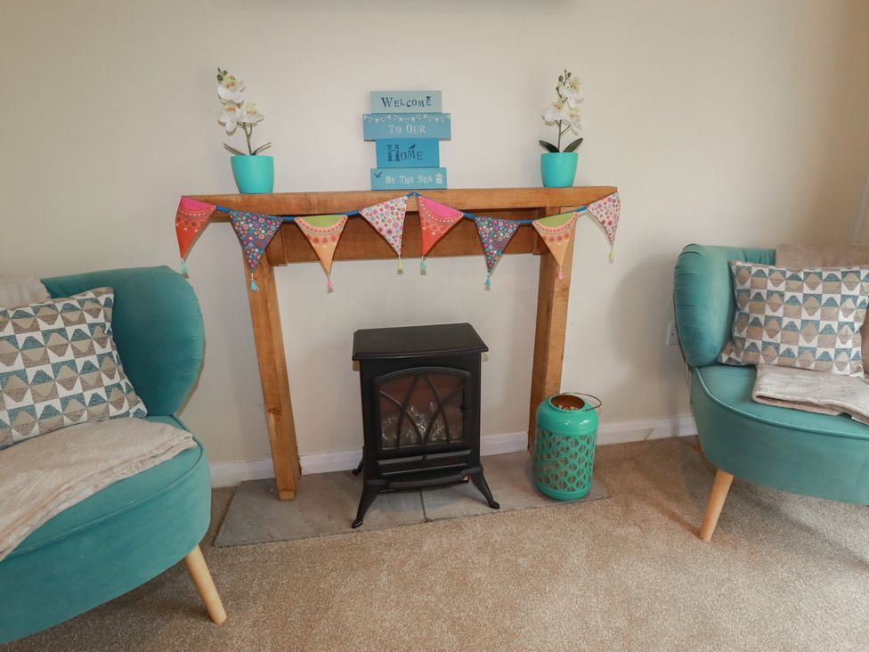 A living room with a fireplace and a decorative banner at Poolside, Atlantic Reach resort, near St Columb Major