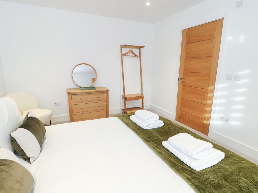 A bedroom with a bed, dresser, mirror, and clothes rack at Glynllifon 4, Marianglas