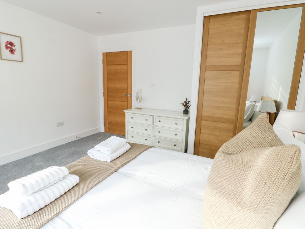 A bedroom with a bed, towels, dresser, and door at Glynllifon 6 in Marianglas