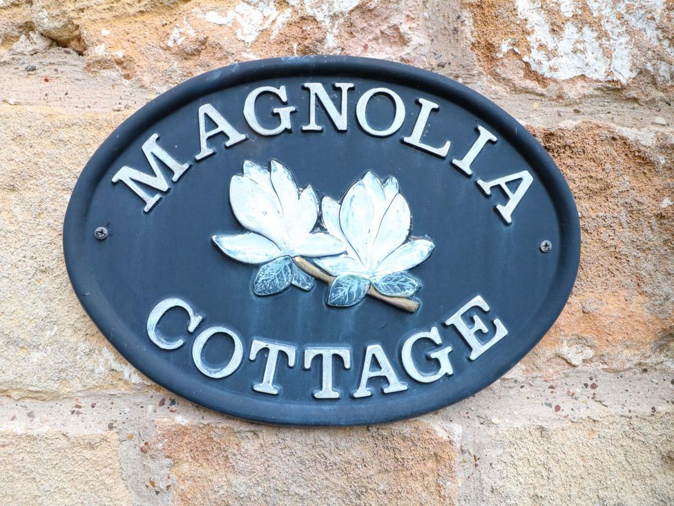 A nameplate sign with 'MAGNOLIA COTTAGE' and magnolia flowers on a stone wall