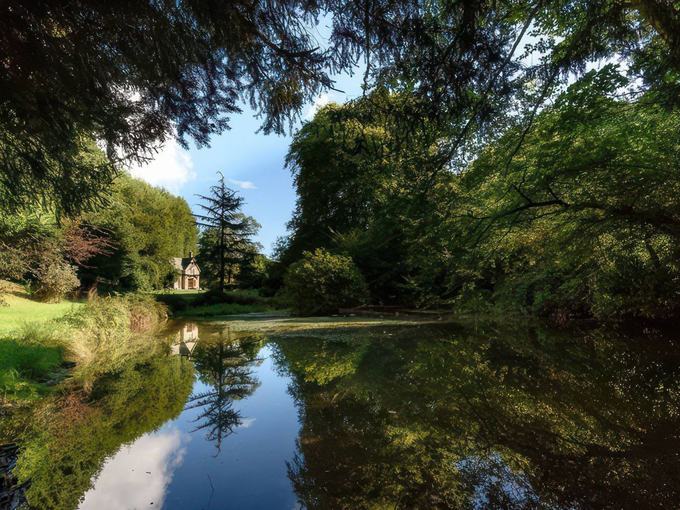 A pond surrounded by trees with a house in the background at Ladye Park in Liskeard