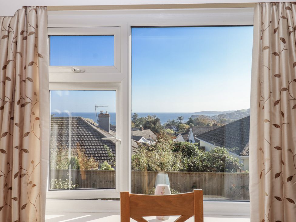 A room with a window overlooking rooftops and ocean at Woodbury, Teignmouth