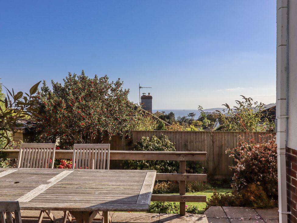 A garden with a wooden table and chairs overlooking the sea at Woodbury in Teignmouth