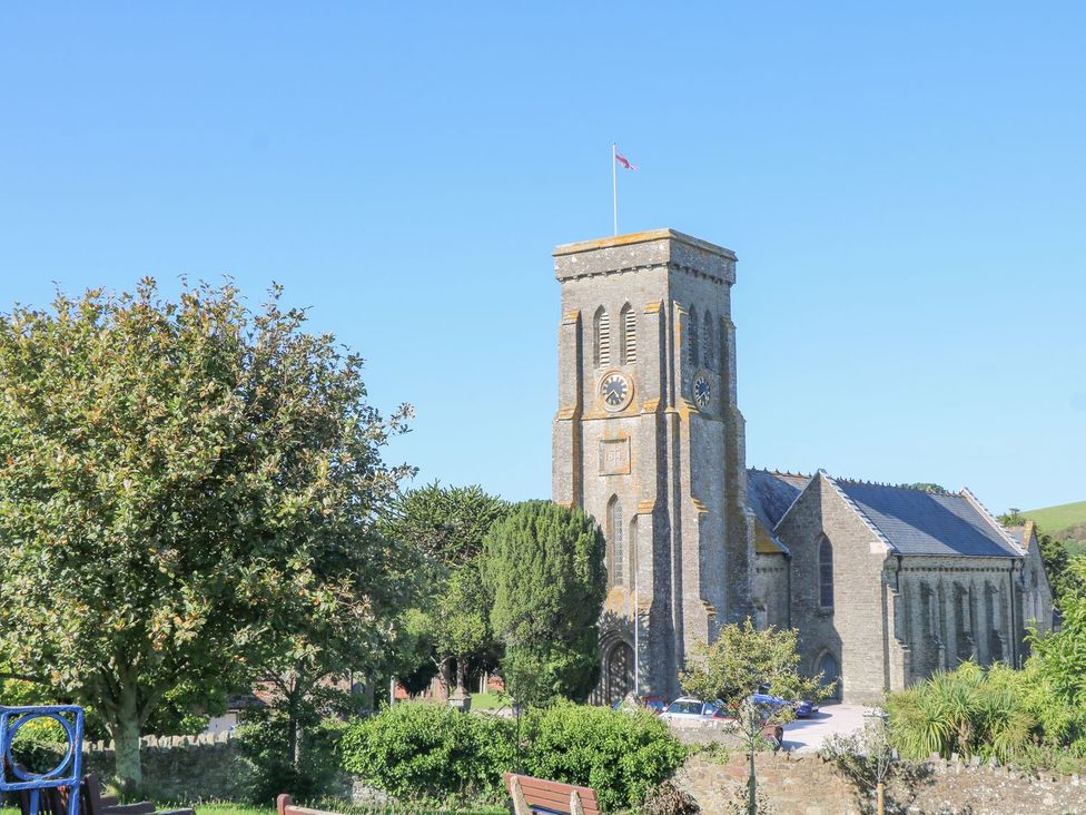 A church with a clock and flag surrounded by trees in Quay Cottage Salcombe