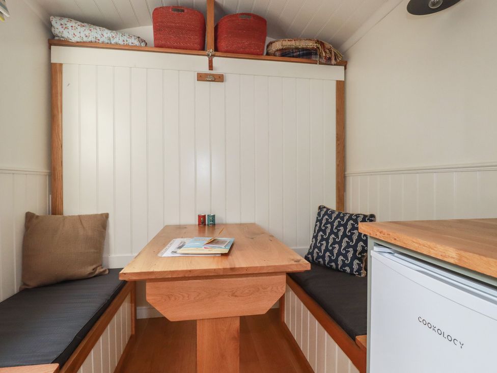 A dining area with a table and cushions at Hillbre Shepherd Hut in Padstow