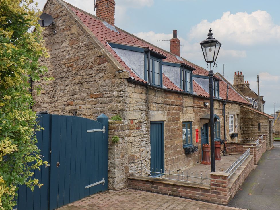 An outdoor view of a stone cottage with a blue gate at Dove Cottage in Sneaton near Ruswarp