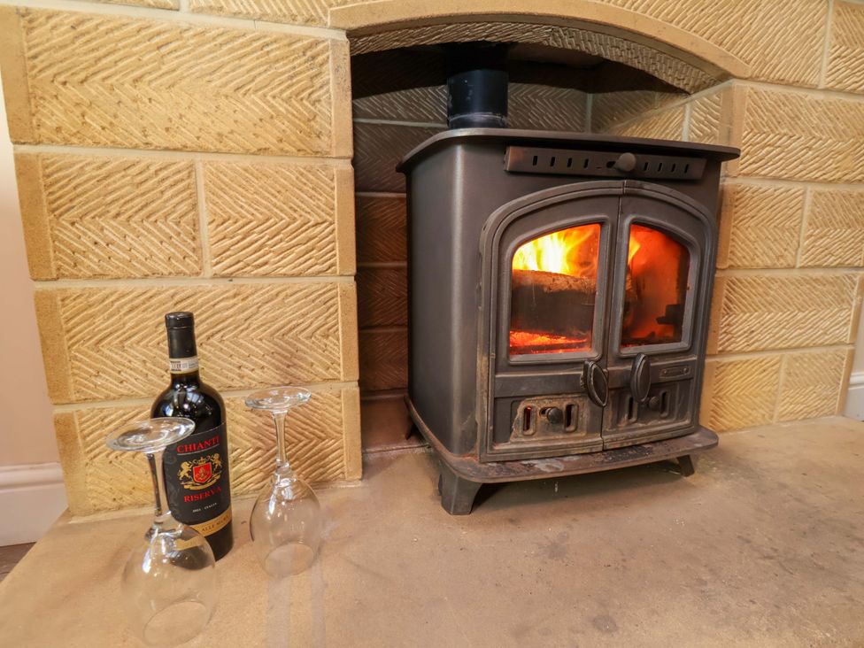 A fireplace with a wood stove and wine glasses at Dove Cottage Sneaton near Ruswarp