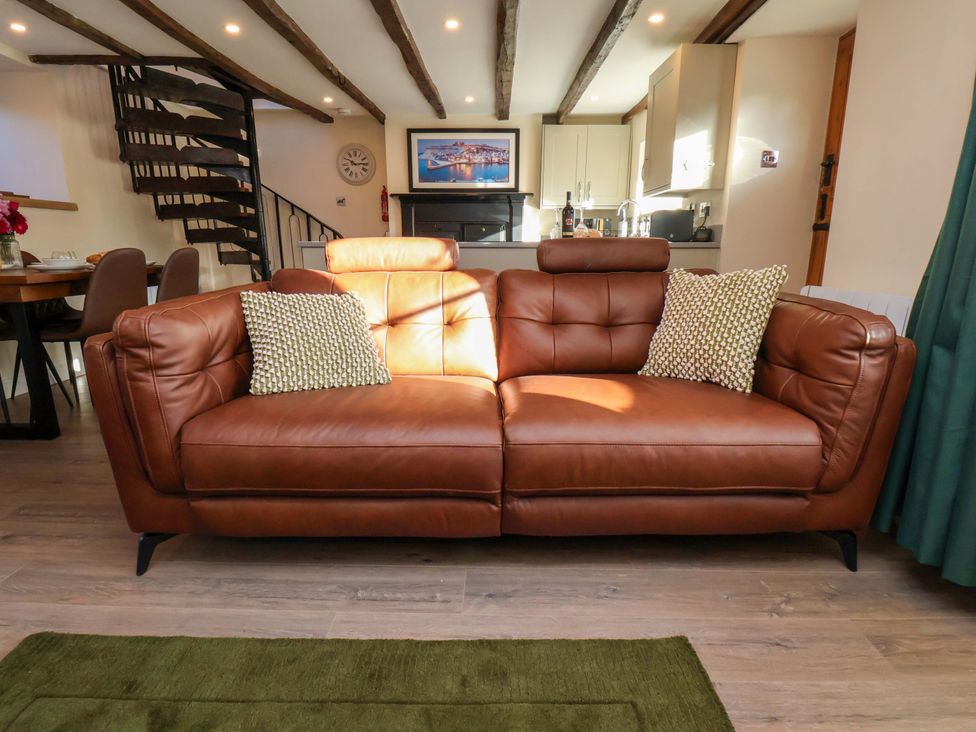 A living room with a brown sofa and dining table at Dove Cottage in Sneaton near Ruswarp