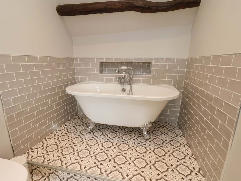 A bathroom with a bathtub and patterned floor tiles at Dove Cottage in Sneaton near Ruswarp