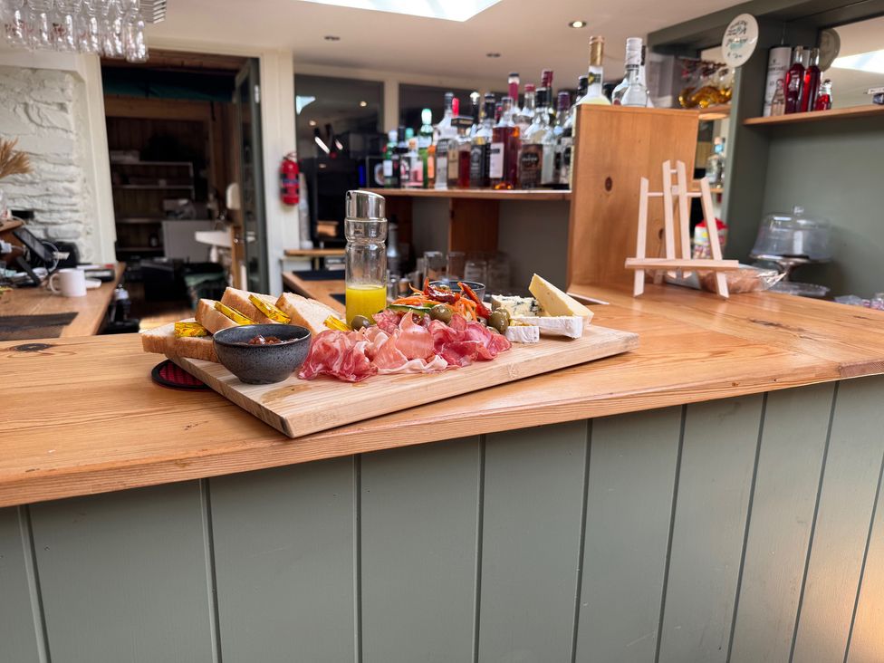 A kitchen with a wooden table displaying cheese, cured meat, bread, and olives at Camnant in Newcastle Emlyn