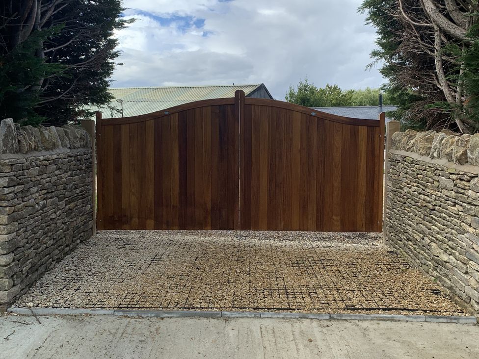 A wooden gate with a stone wall and gravel driveway at Rose Stables in Black Bourton near Bampton