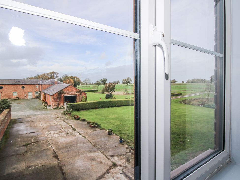 A view from a window overlooking a field and brick buildings at Garden Cottage in Ellesmere