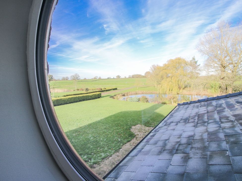 A view of a field and pond from a circular window at Garden Cottage in Cockshutt
