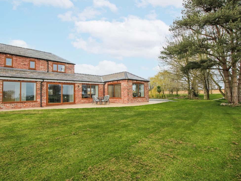 An outdoor view of a brick house with a patio and surrounding grass at Garden Cottage in Cockshutt