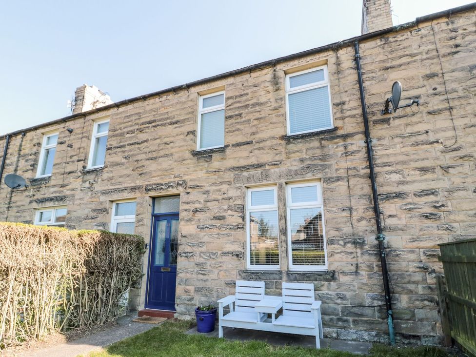 A house exterior with a blue door and seating at 23 Northumbria Terrace Amble