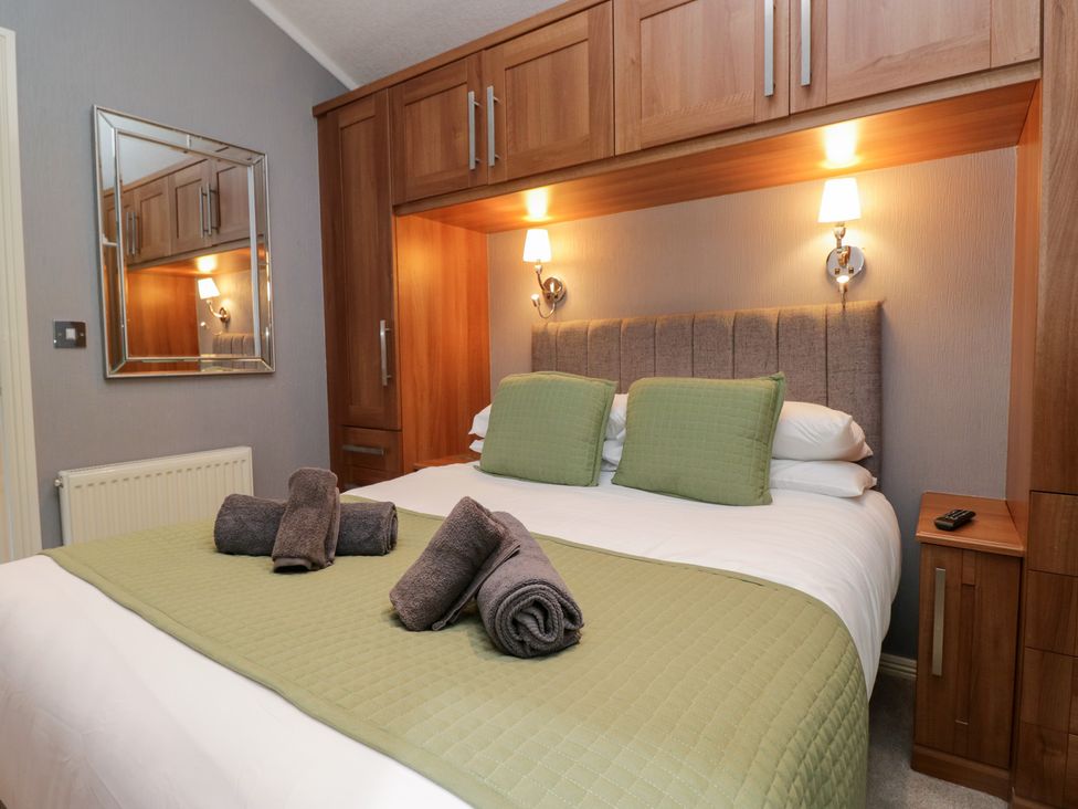 A bedroom with a double bed and wooden storage at 32 Grasmere, White Cross Bay near Windermere