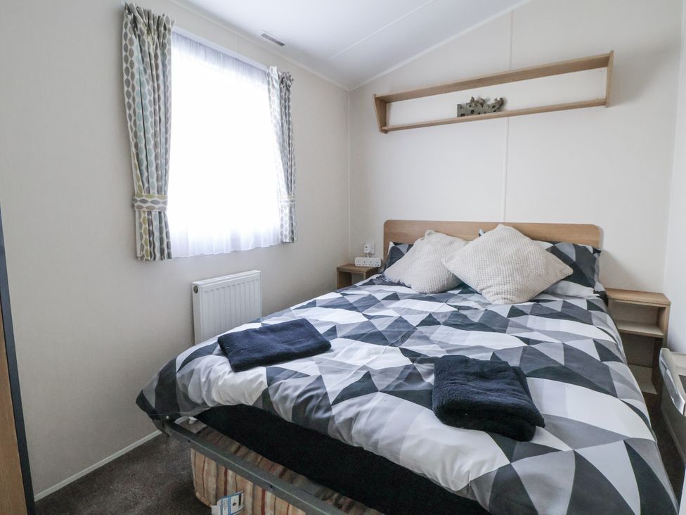 A bedroom with a bed and shelf at Chappie's Caravan - Rhyl
