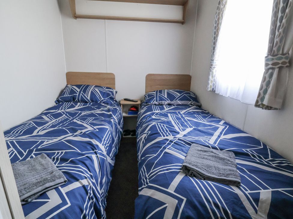 A bedroom with two beds and a shelf at Chappie's Caravan - Rhyl