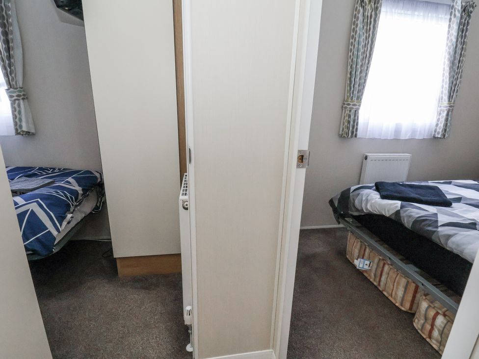 A bedroom with beds and curtains at Chappie's Caravan - Rhyl