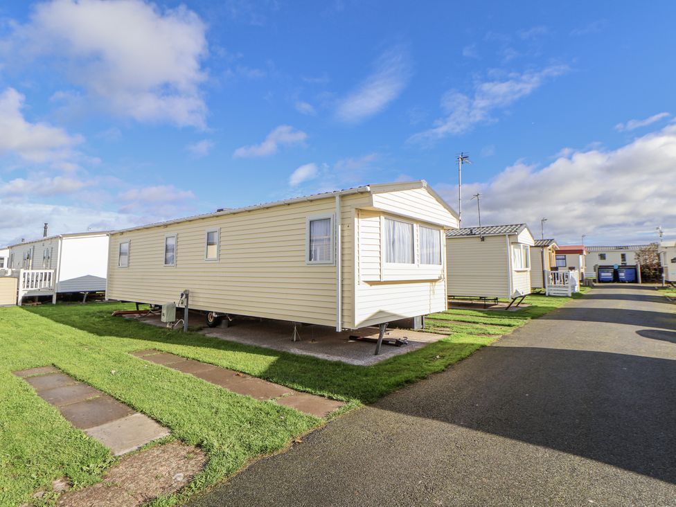 A yellow caravan on grass with a path and road at Chappie's Caravan - Rhyl 8 Rhyl