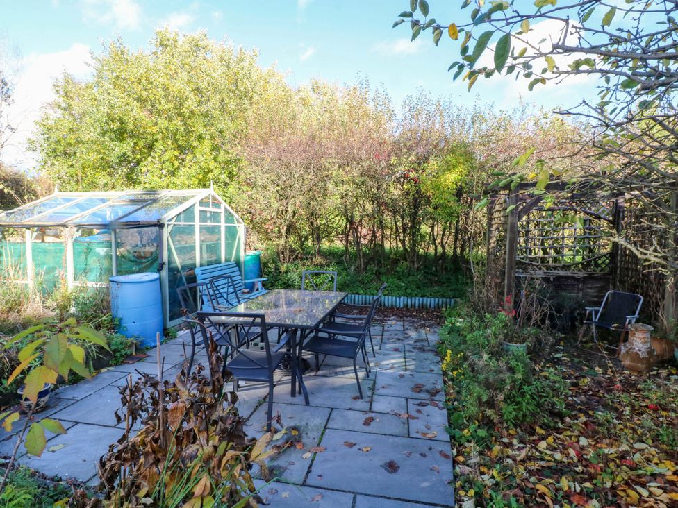 A garden with a table and chairs near a greenhouse at Pineapple Cottage