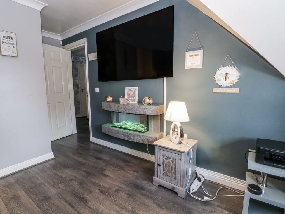 A living room with a television mounted on the wall and a table with a lamp at 24 Wilmslow Court, Wilmslow