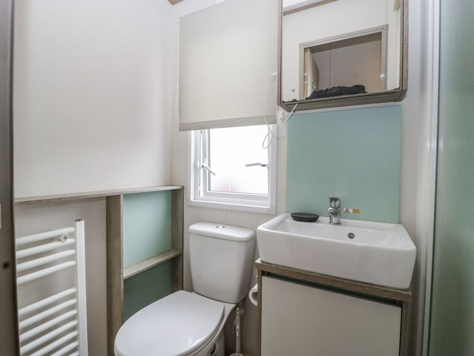 A bathroom with a toilet, sink, mirror, and window at Caravan - 2 Bayside Watchet