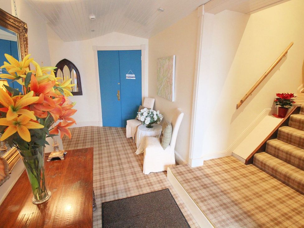A hallway with stairs leading up and a table with flowers at Newton Hall in Inveraray