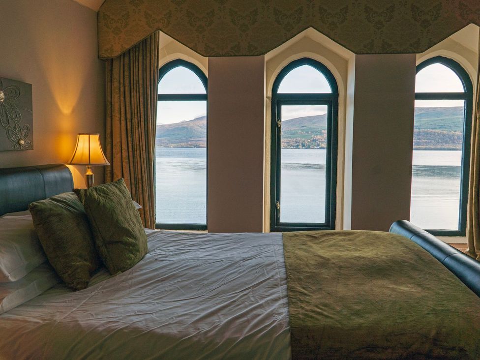 A bedroom with a bed and windows overlooking a lake at Newton Hall in Inveraray