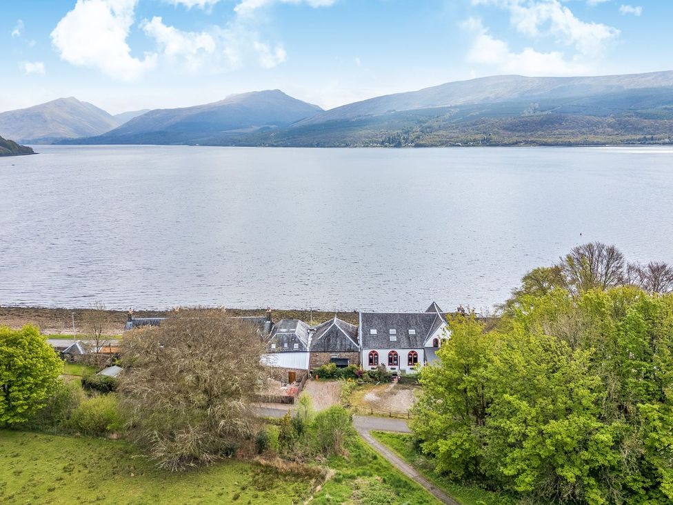 A view of a house by a lake surrounded by mountains at Newton Hall in Inveraray