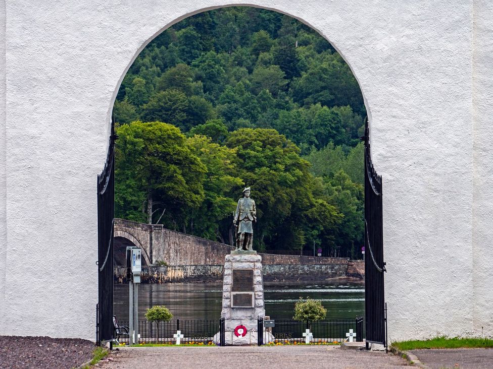 A statue framed by an arch overlooking water and trees at Newton Hall in Inveraray