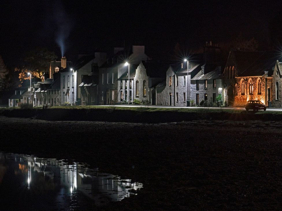 A row of houses at night with reflections in the water at Newton Hall in Inveraray