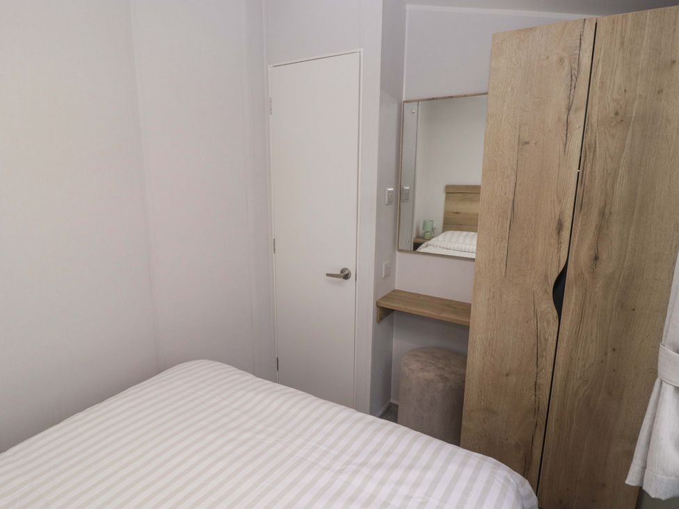 A bedroom with a bed, wardrobe, mirror, desk and stool at 47 Chestnut Road in Porthcawl