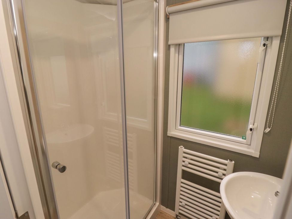 A bathroom with a shower, sink, and window at 47 Chestnut Road Porthcawl