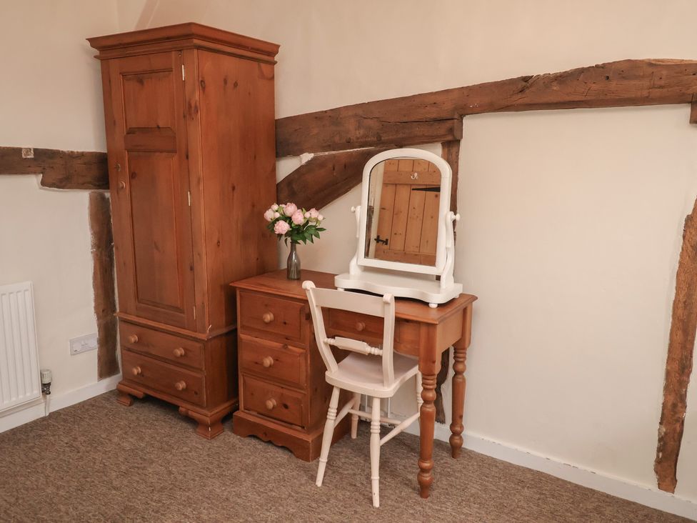 A bedroom with a wardrobe, dresser, mirror, and flowers at Duke Cottage in Woodbridge