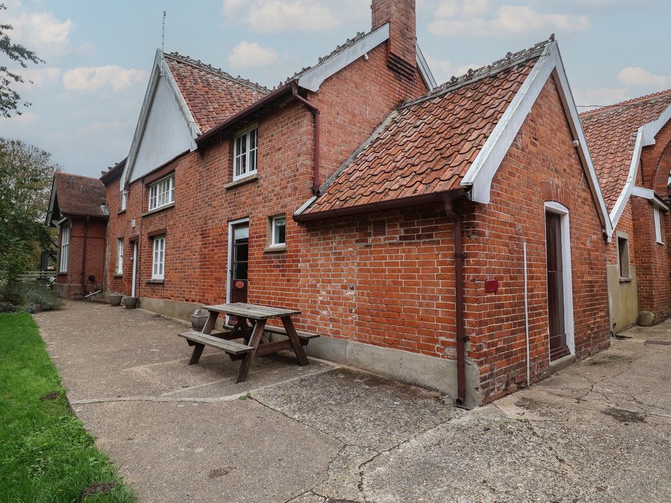 An outdoor view of a brick house with a table and bench at Duchess Cottage Woodbridge