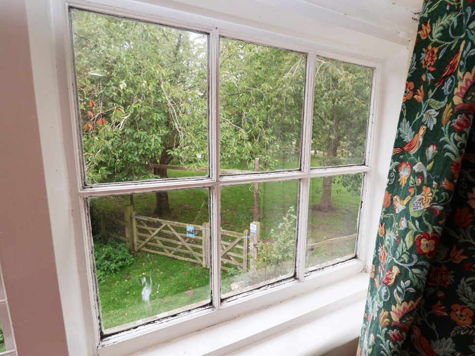 A window with a view of trees and a gate at Duchess Cottage Woodbridge