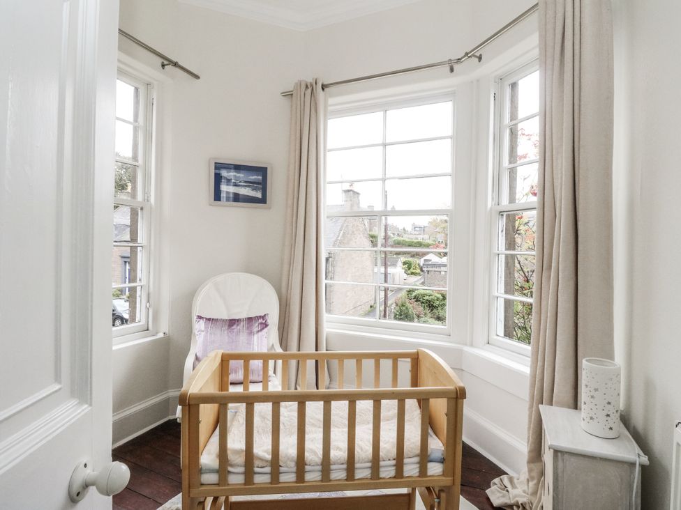 A bedroom with a baby crib and a chair at Rowan Tree House in Brechin